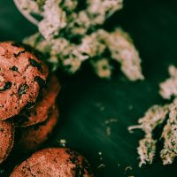 The concept of marijuana in food. Treatment with the help of Canabis in a moody green tone. Chocolate Cookies with CBD and THC are on a black table with cannabis buds.